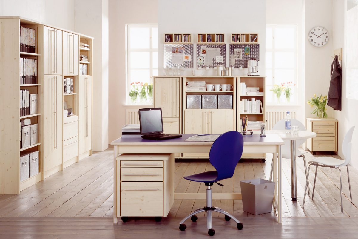 Ein hell eingerichtetes HomeOffice mit gefüllten Schränken und einem Schreibtisch mit blauer Tischplatte und einem passenden blauen Stuhl